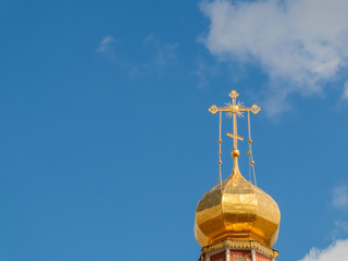 The Golden dome of an Orthodox temple on background of blue sky and clouds. Golden cross on the dome of the temple.