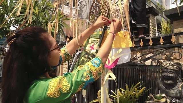 Balinese woman in traditional ceremony costume decorating penjor on Galungan day (Bali holiday ceremony). Medium shot with Sony a7s on tripod on sunny day