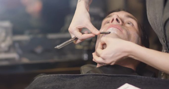  Close up of man getting a shave with razor in traditional barber shop. 