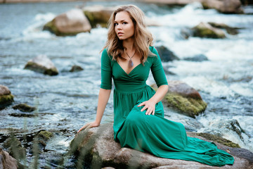 Beautiful girl posing on rocks near the water. Model in a green dress in nature.