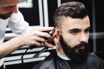 Master cuts hair and beard of men in the barbershop, hairdresser makes hairstyle for a young man