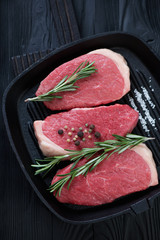 Cast-iron grill pan with fresh uncooked beef medallion steaks, high angle view, vertical shot