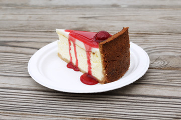 Slice of cheesecake topped with cherry compote on plate on brown table with dessert, top view