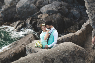 The bride and groom on nature in the mountains near the water. Suit and dress color Tiffany. Kiss and hug.