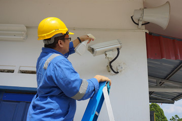 A male worker doing a maintenance work by cleaning and inspecting security camera.