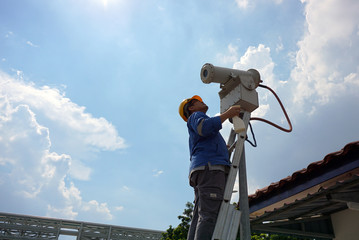 A male worker doing a maintenance work by cleaning and inspecting security camera.