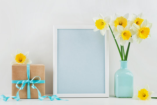 Mockup of picture frame decorated narcissus or daffodil flowers in vase and gift box for greeting on mother or woman day.