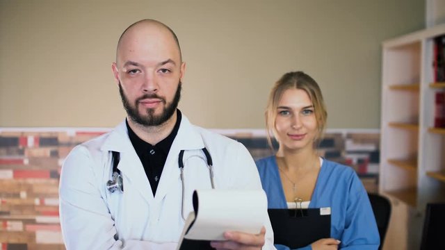 Adult 30s male doctor man with a 20s female nurse in uniform are posing at medical office 4k