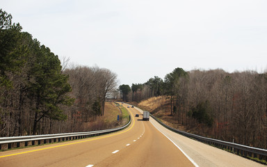 A winding and hilly interstate with a few cars driving through a spring countryside landscape
