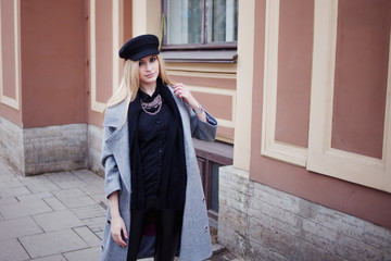 Young, hip and attractive blonde walking around the city, girl in a stylish hat and a gray coat