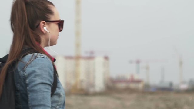 Beautiful young girl with a backpack, denim jacket, plaid shirt, appears in frame, left to right. Medium Shot