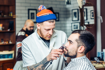 portrait of handsome man with beard in barbershop. barber working with electric razor