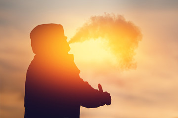 Close-up A man vape smokes an electronic cigarette against the sunset. The steam is falling. Concept Abandonment of tobacco. high contrast and monochrome color tone.
