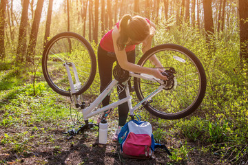 Fototapeta premium Young woman repairing a bicycle in the forest