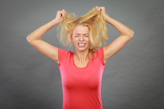 Frustrated woman holding her damaged blonde hair