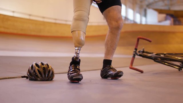  Man with prosthetic leg at cycling track attaches limb and prepares to train