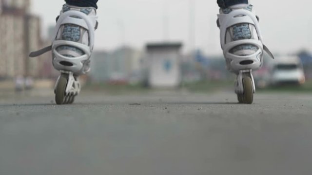 Girl rides on rollers on asphalt in background of city. Close Up Shot