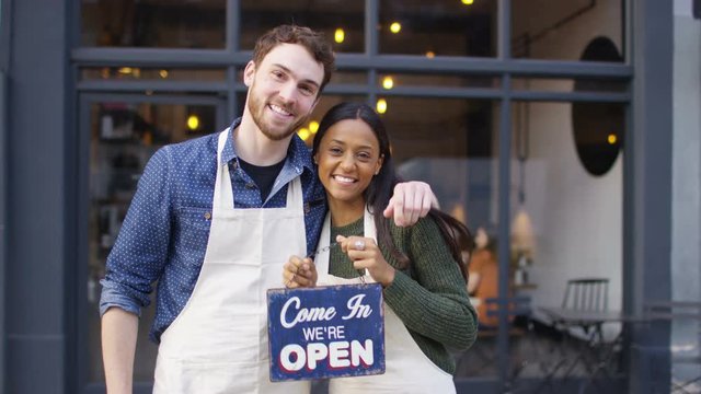  Happy owners outside cafe hold up a sign to show they are open for business. 