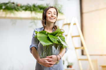 Young woman planting home with greenery standing with big plant in the room