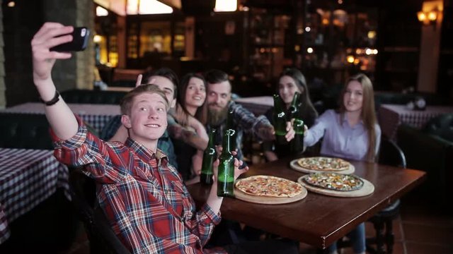 The guy makes a friend company in pizzeria. A company of friends resting in a pizzeria and making selfie on the background of pizza and beer