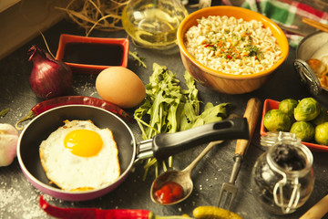 Table with food in breakfast or lunch: omelette, cabbage, oil, chili, ketchup, arugula, onion, garlic, noodles, cucumber, coffee, biscuits, orange, bread and butter