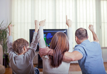 Naklejka na ściany i meble Family watching sports on TV and cheering.