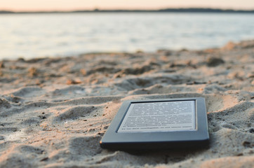 E-book reader on the beach sand. Lorem ipsum text used. Copy space. 