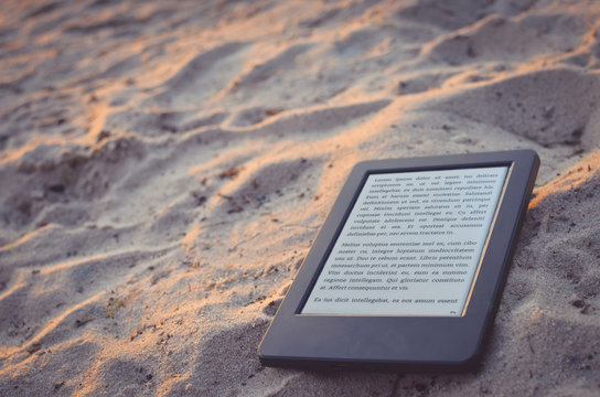 E-book reader on the beach sand. Lorem ipsum text used. Copy space. Toned image