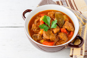 Goulash in ceramic bowl on white wooden background. Traditional hungarian soup.