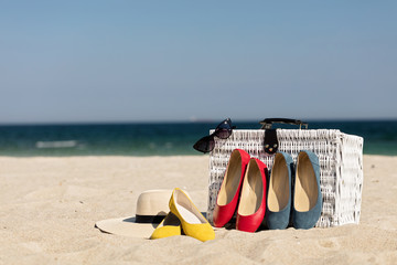 Summer vacation at sea. White wicker suitcase and women's accessories and shoes on the beach.