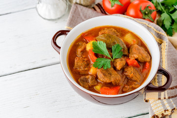 Goulash in ceramic bowl on white wooden background. Traditional hungarian soup.