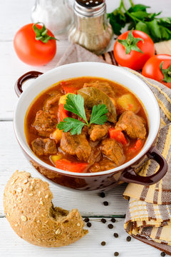 Goulash in ceramic bowl on white wooden background. Traditional hungarian soup.