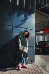 fashion closeup portrait of nice pretty young hipster woman posing in sunglasses Outdoor .Brunette happy girl in green raincoat and pink sneakers walks the street of the city.