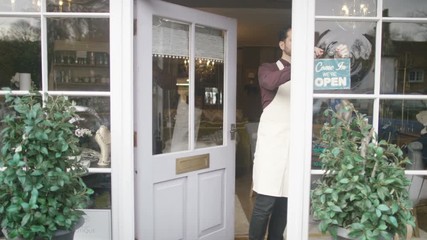 Cheerful business owner outside his shop turns sign around to show he is open - Powered by Adobe