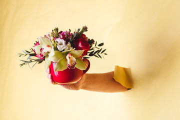 Hand holds small vase with flowers and lily breakes through a yellow background