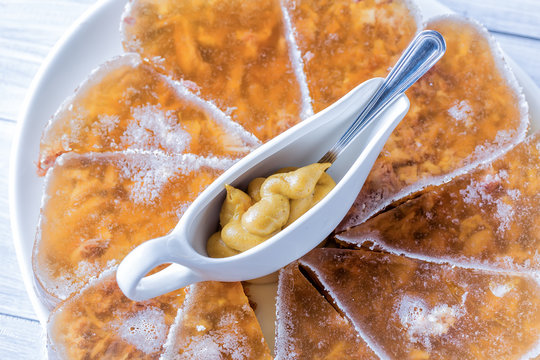 Jellied meat with mustard in a bowl and spoon on white plate close up