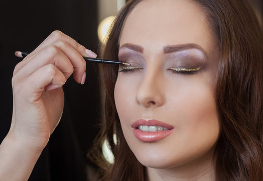 The make-up artist paints eyes with eye shadow in the beauty salon.