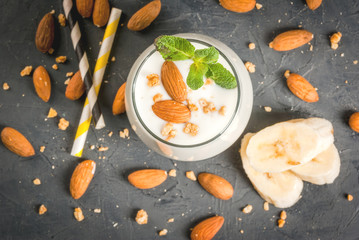 Fototapeta na wymiar Healthy food. Dietary breakfast or snack. White smoothies made from yogurt, banana and almond nuts. decorated with mint. On a dark concrete table with ingredients, striped straws. Copy space