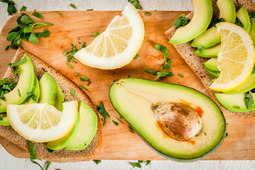 Healthy diet food. Spring meal. Sandwiches of black bread with avocado, lemon and greens. With ingredients on cutting board on white stone table