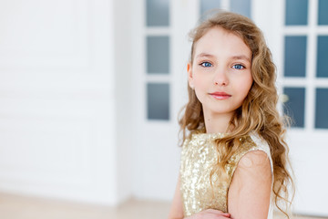 A portrait of a beautiful girl with long curly blond hair and blue eyes wearing a gold fashionable dress and high-heeled shoes