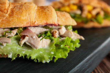 Wooden board with chicken salad in croissant bun, closeup