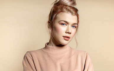 Young woman  with natural make-up  in soft powdery beige pastel colors in a peach sweatshirt on a beige background