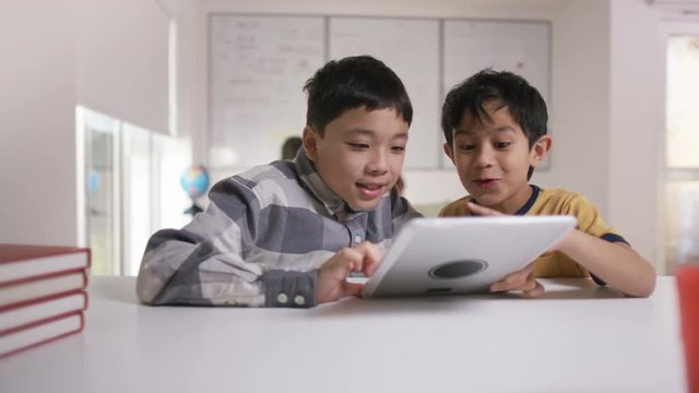 Happy little boys working on computer tablet in school classroom