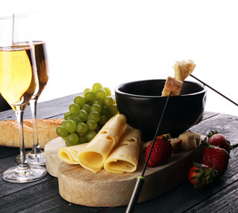 Gourmet Swiss fondue dinner with assorted cheeses on a board and strawberries alongside a heated...