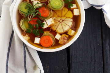 Broth with carrots, onions various fresh vegetables in a pot - colorful fresh clear spring soup. Rural kitchen scenery vegetarian bouillon or stock