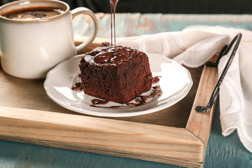 Pouring melted chocolate onto tasty cocoa brownie on plate