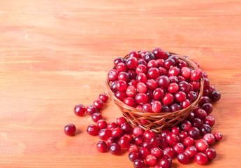 Basket with ripe cranberries on a wooden background