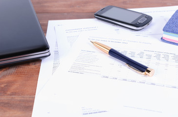 business accessories - a pen, a phone and laptop on Desk with financial documents