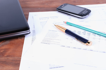 Business accessories - a pen, a phone and a laptop lying on tax documents