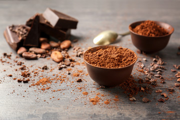 Bowl with aromatic cocoa powder and pieces of chocolate on table